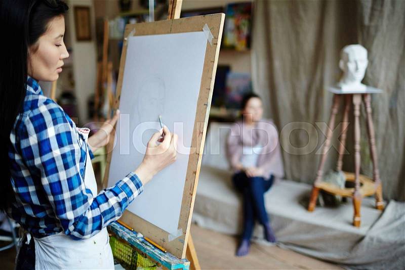 Young student drawing face of girl with pencil in workshop, stock photo