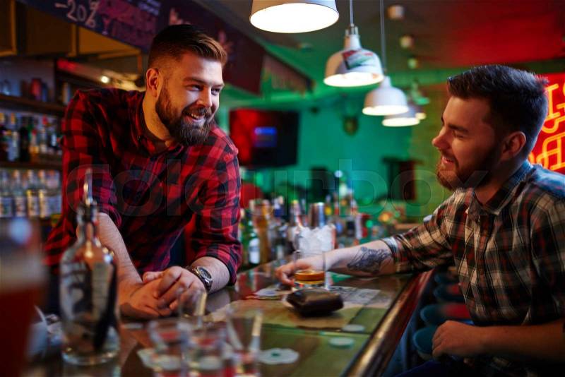 Happy barman and his friend talking in pub after-hours, stock photo