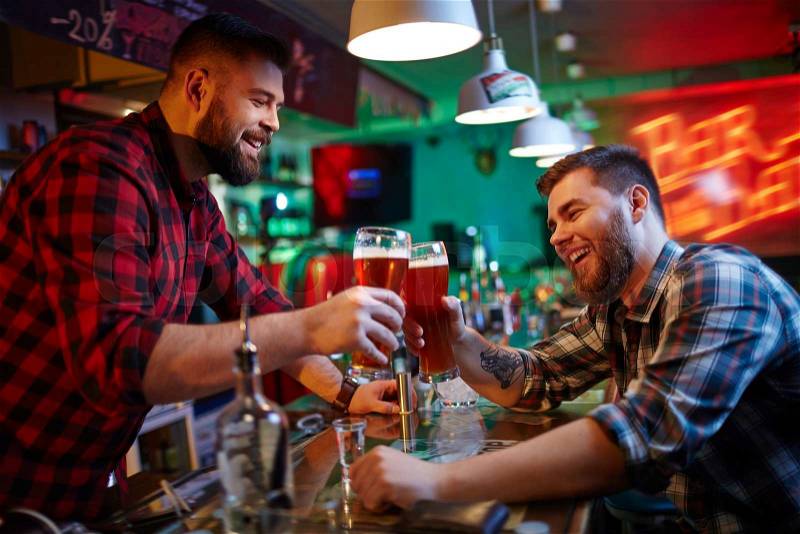 Happy barman and his friend clinking with glasses of beer, stock photo