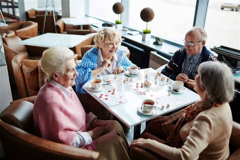 Group of friendly seniors playing lotto in cafe, stock photo
