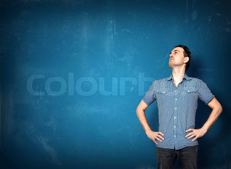 Man looking left on a blue grunge wall with his hands in the side, stock photo
