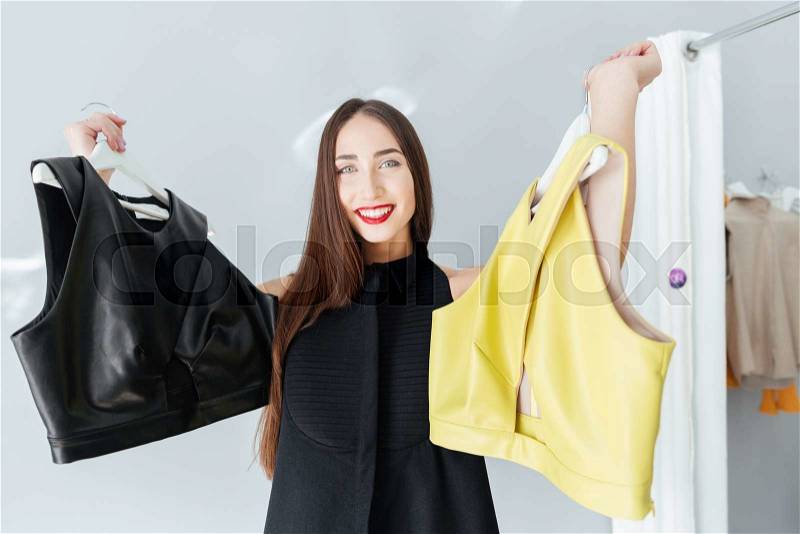 Cheerful woman choosing between two jacket in store, stock photo