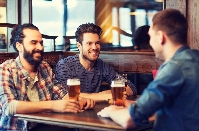 People, men, leisure, friendship and communication concept - happy male friends drinking beer at bar or pub, stock photo