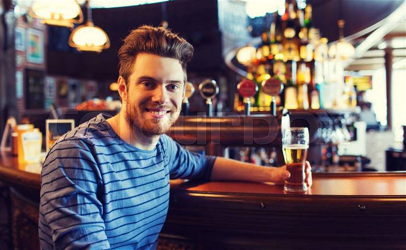 People, drinks, alcohol and leisure concept - happy young man drinking beer at bar or pub, stock photo
