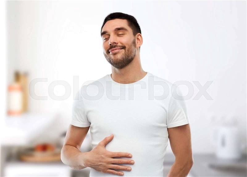 Eating, satisfaction and people concept - happy full man touching his tummy over kitchen background, stock photo