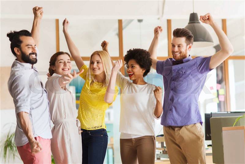 Business, triumph, gesture, people and teamwork concept - happy international creative team raising hands up and celebrating victory in office, stock photo