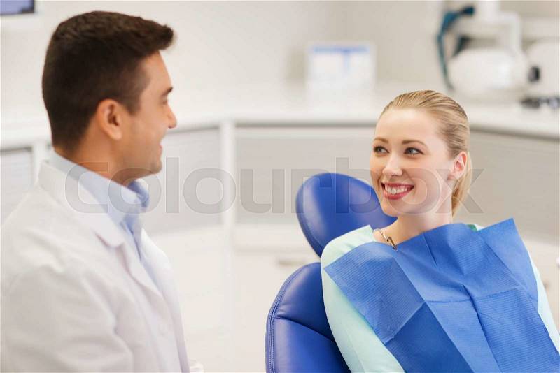 People, medicine, stomatology and health care concept - happy male dentist with woman patient talking at dental clinic office, stock photo