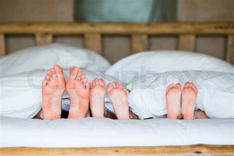 Family with two kids laying in bed with their feet forward, stock photo