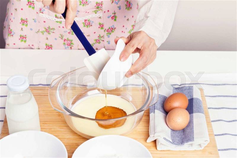 Woman pouring honey into milk for mixing baking ingredients for healthy muffin, stock photo
