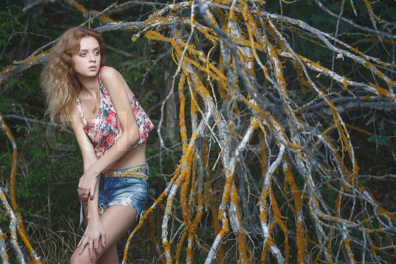 Young sexy woman model in jeans and tank top posing for fashion portrait near old weathered branches, stock photo