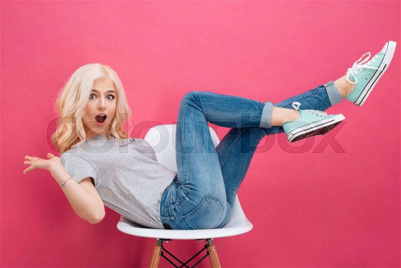 Cheerful woman sitting on the chair with raised legs over pink backgorund, stock photo