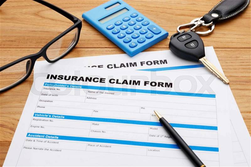Insurance claim form with pen and car key on wood desk, stock photo