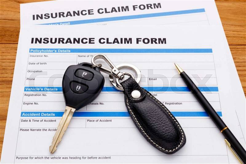 Insurance claim form with car key and pen on wood desk, stock photo