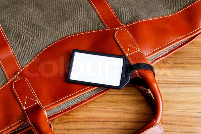 Travel bag with blank tag on wood table, stock photo