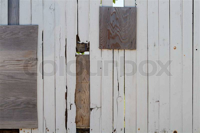 A heavily repaired wooden plank fence around industry area. You can just see a few leaves and some grass through the holes of the fence, stock photo
