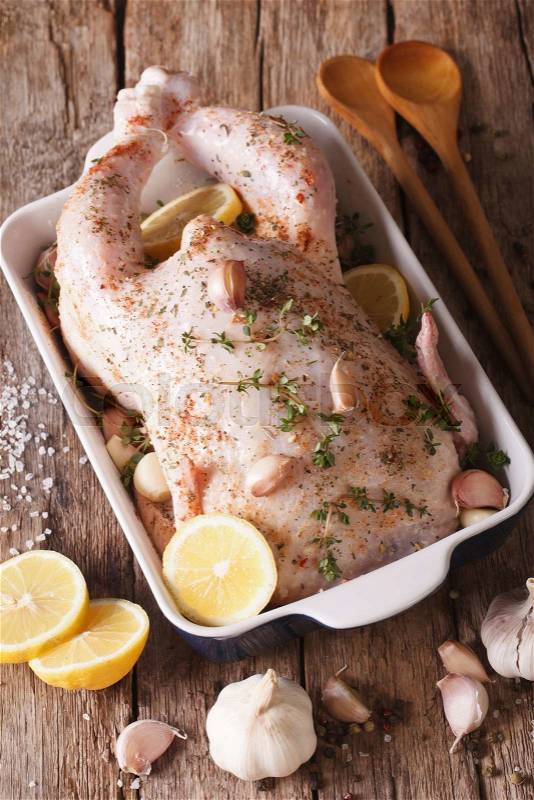 Raw whole chicken marinated with garlic, thyme and lemon close-up on the table. Vertical\, stock photo