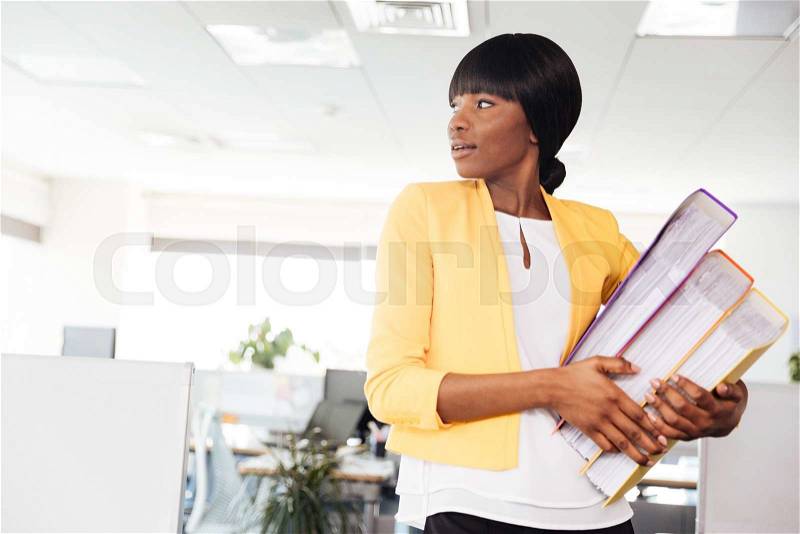 Afro american businesswoman holding folders and looking away in office, stock photo