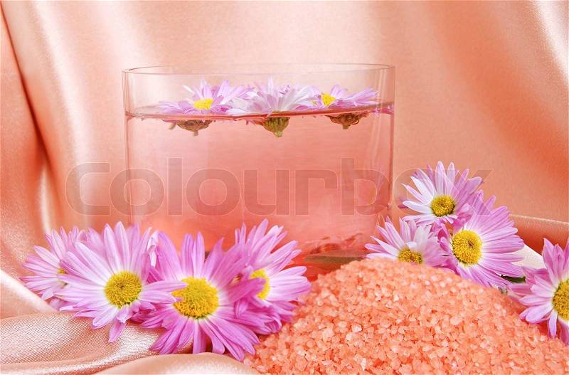 A bright pink spa and body care background. Salt and flower floating in glass bowl, stock photo