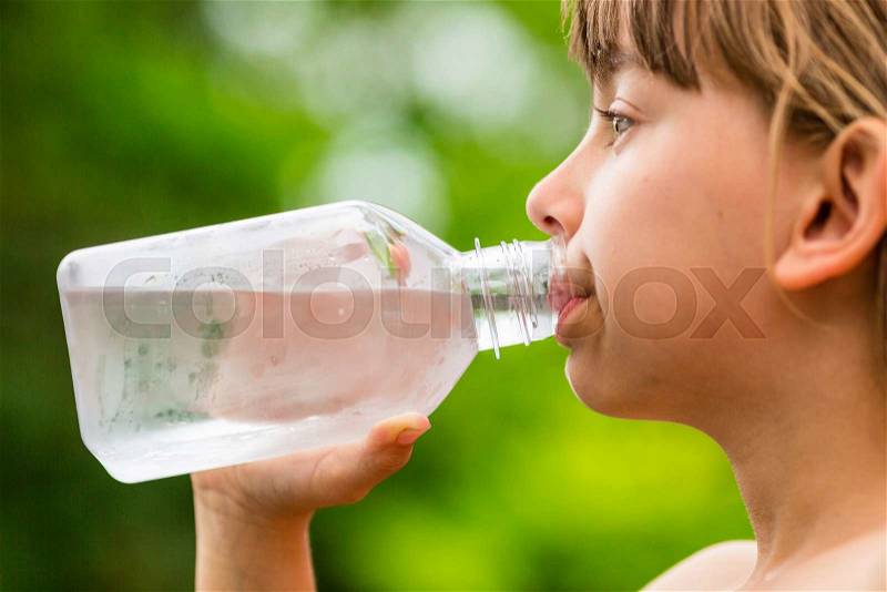 Closeup of young child drinking pure tap water from transparent plastic drinking bottle while outdoors on a hot summer day, stock photo