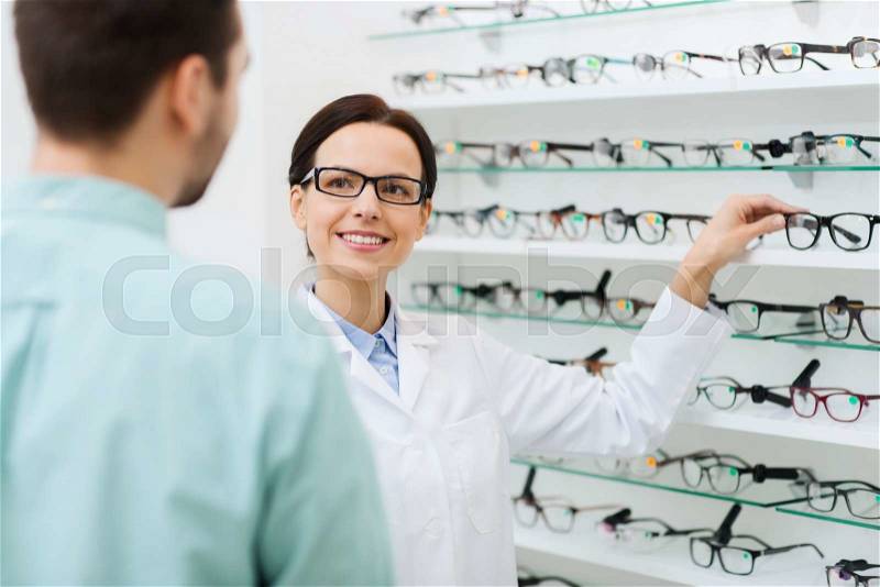 Health care, people, eyesight and vision concept - female optician showing glasses to man at optics store, stock photo
