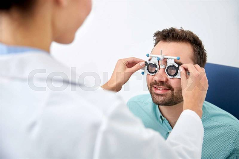 Health care, medicine, people, eyesight and technology concept - optometrist with trial frame checking patient vision at eye clinic or optics store, stock photo