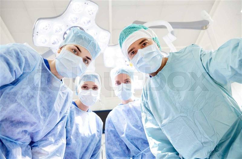 Surgery, medicine and people concept - group of surgeons in operating room at hospital looking into camera, stock photo