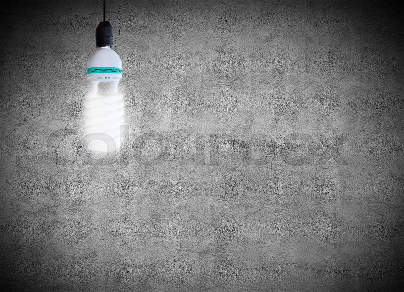 Energy saving fluorescent light bulb on a gray concrete wall background, stock photo