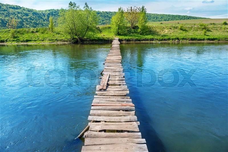 Old wooden bridge through the river with green trees on the banks, stock photo