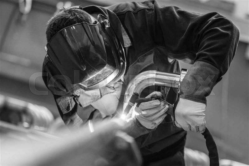Industrial worker with protective mask welding inox elements in steel structures manufacture workshop. Black and white photo, stock photo