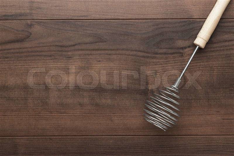 Retro egg whisk with wooden handle on brown table with copy space, stock photo