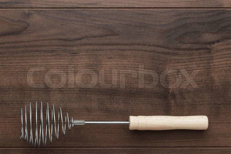 Retro egg whisk with wooden handle on brown table with copy space, stock photo