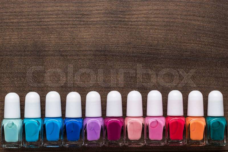 Nail polish bottles of different colors on brown wooden table, stock photo