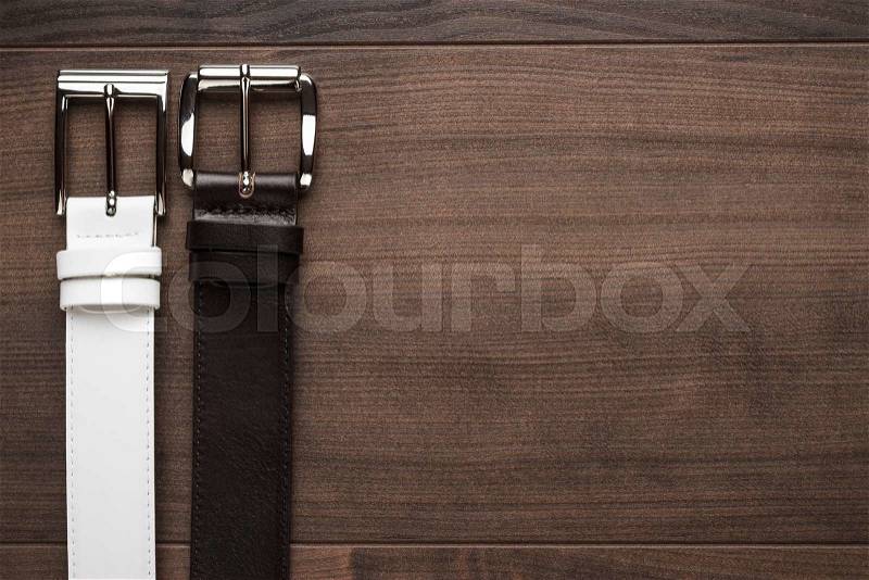 Brown and white men\'s leather belts on wooden table, stock photo