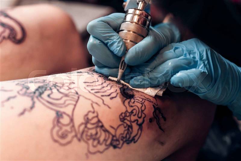 Closeup tattoo artist fill circuit tattoo in a professional salon. Leg with a pattern and black paint. Master works in black sterile gloves. , stock photo