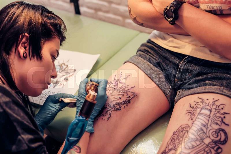 Professional tattoo artist doing tattoo. Portrait of a woman tattoo master showing a process of creation tattoo on a legs. Tattooist machine,gun. Free space to fill,text, stock photo