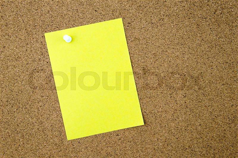 Blank yellow paper note pinned on cork board with white thumbtack, copy space available, stock photo