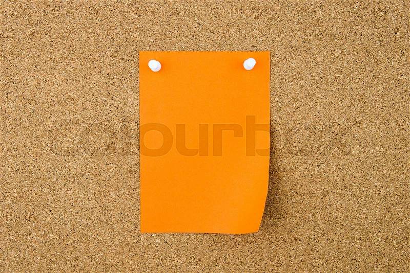 Blank orange paper note pinned on cork board with white thumbtacks, copy space available, stock photo