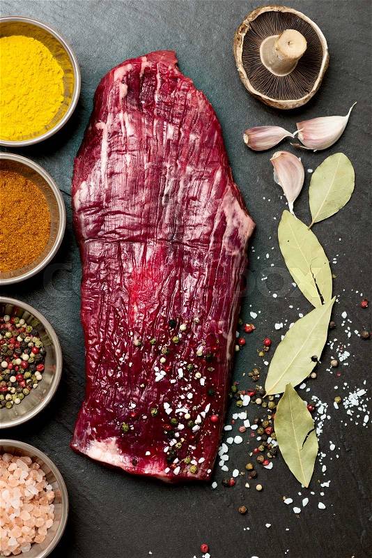 Spices in bowls and raw flank steak on stone background, stock photo