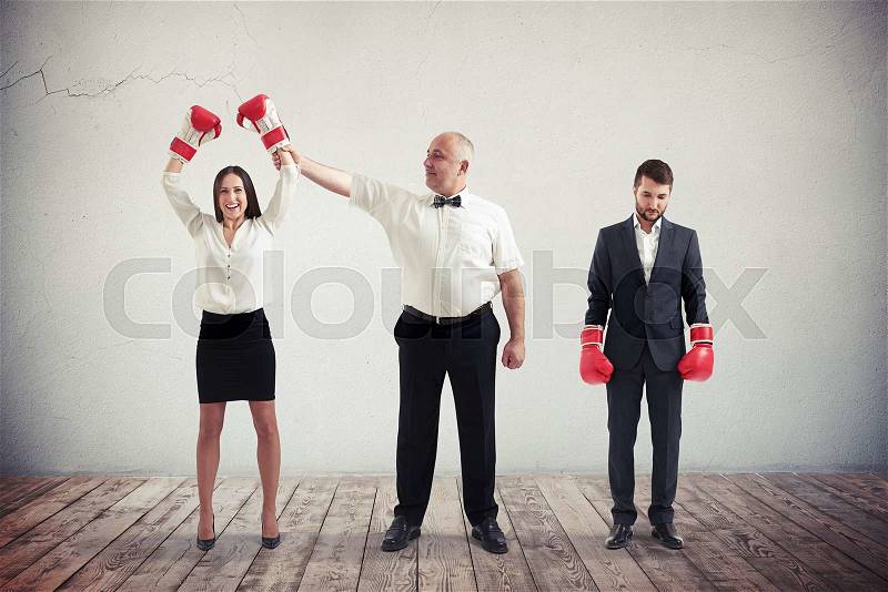 The referee is announcing the winner after a boxing match - it is the businesswoman and boxing gloves with her fists raised, while the businessman is the loser, stock photo