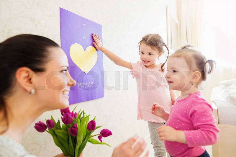 Mothers day, cute little girls giving flowers and greeting card to their mum, stock photo