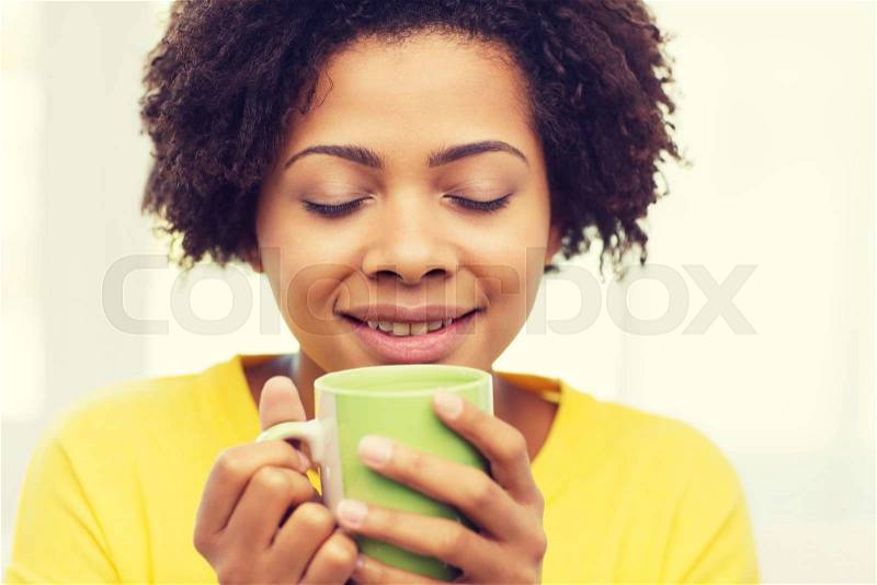People, drinks and leisure concept - happy african american woman drinking tea from cup or mug at home, stock photo