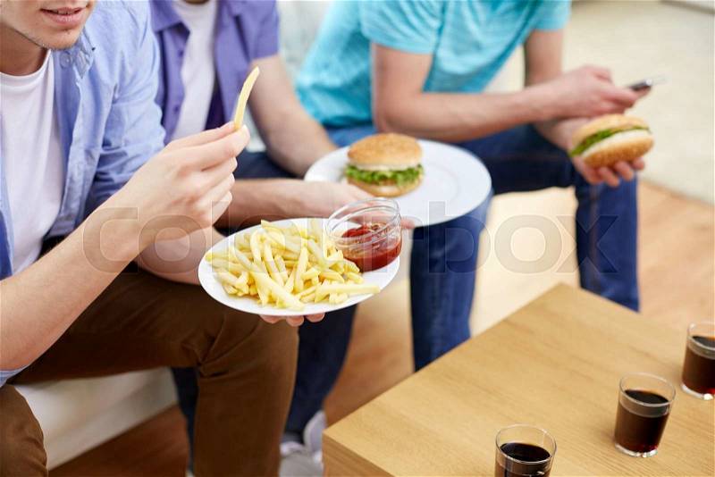 Fast food, unhealthy eating, people and junk-food - close up of happy friends eating french fries and hamburgers at home, stock photo
