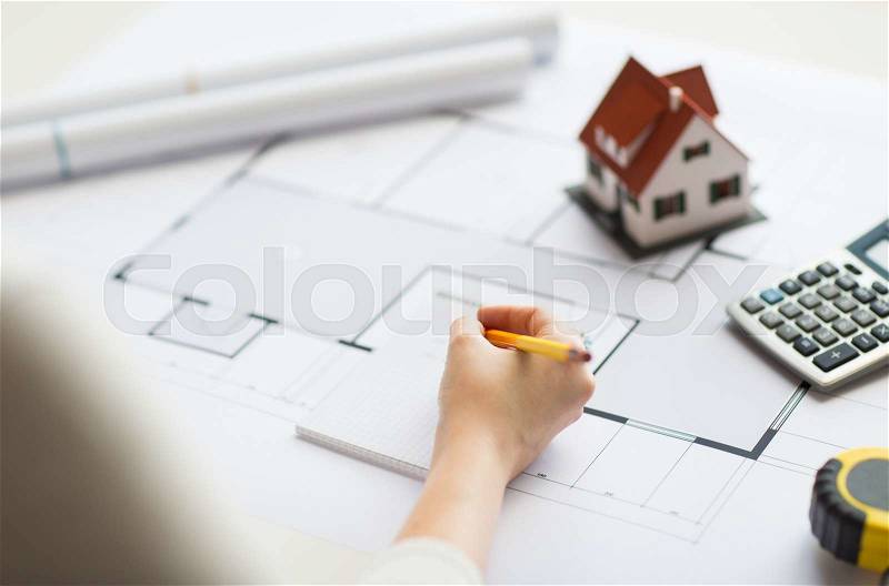 Business, architecture, building, construction and people concept - close up of architect hand with blueprint and architectural tools writing to notebook, stock photo