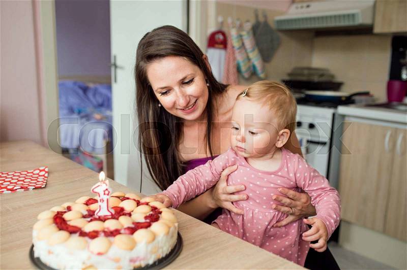 Young mother holding her cute baby daughter with birthday cake, stock photo