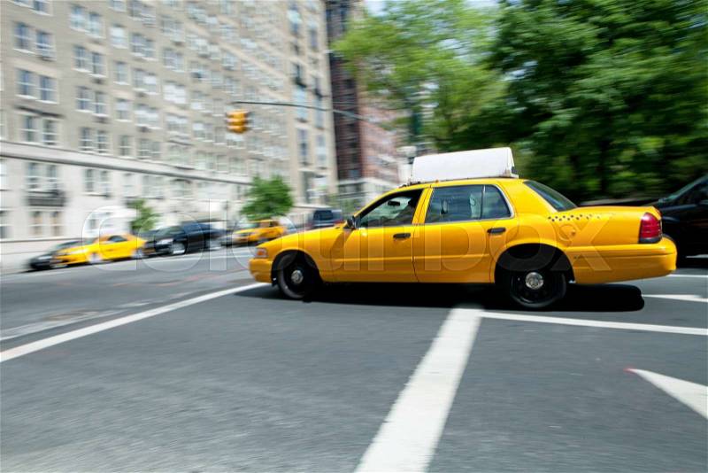 Yellow NYC taxi cab speeding by during daytime. Slow shutter speed panning technique used for motion blur, stock photo