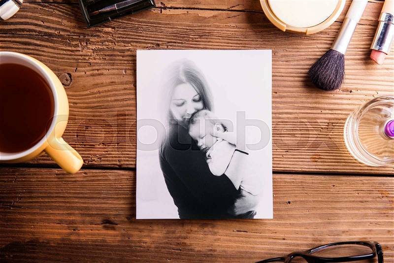 Mothers day composition. Black-and-white picture of mother holding her little baby, cup of coffee and various make up products. Studio shot on wooden background, stock photo