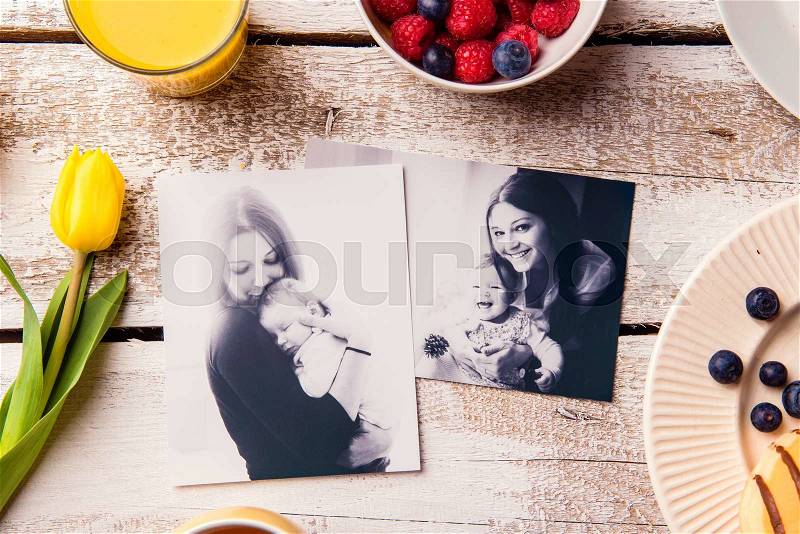 Mothers day composition. Black-and-white pictures of mother holding her little baby daughter and a breakfast meal. Studio shot on wooden background, stock photo
