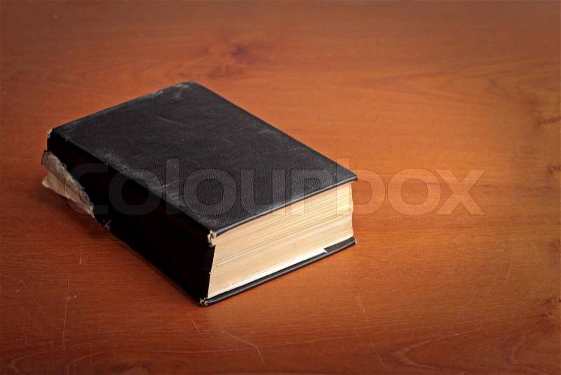 Old black covered book on the brown scratched table, stock photo