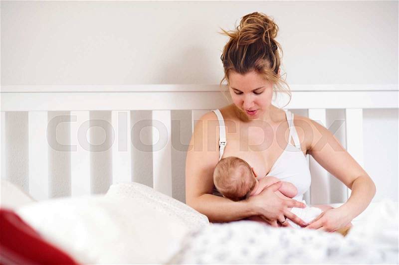 Young mother breastfeeding her cute newborn baby son, home bedroom, stock photo