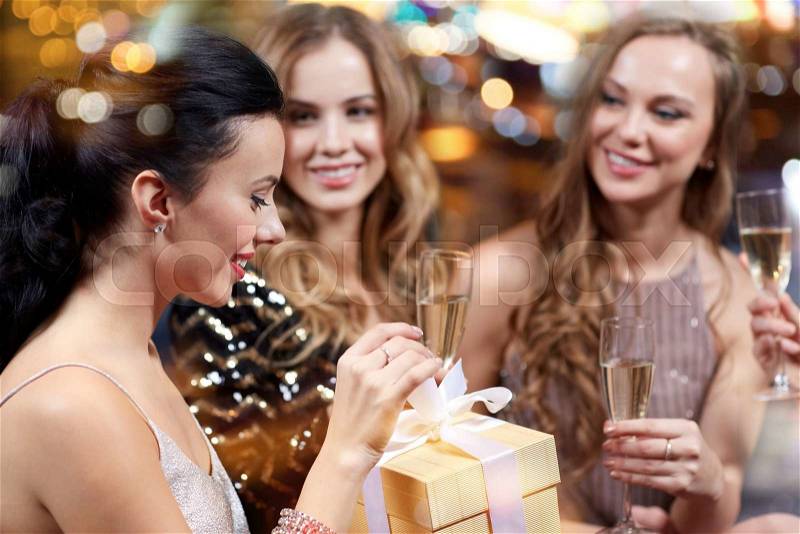 Celebration, friends, bachelorette party, birthday and holidays concept - happy women with champagne glasses and gift box at night club, stock photo